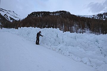 a man stood next to a deep pile of avalanche debris
