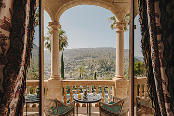 A balcony with two chairs and a table with a drink on it