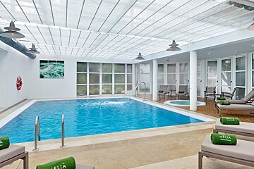 Bright indoor pool area with a jacuzzi, lounge chairs, and a translucent roof. The modern space offers a serene, spa-like atmosphere.