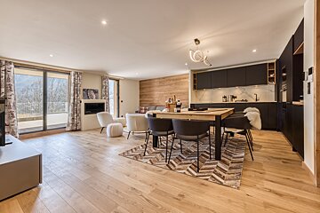 Chic open-plan chalet interior featuring a modern kitchen, dining area, comfy lounge, light wood accents, and large windows showcasing mountain scenery.