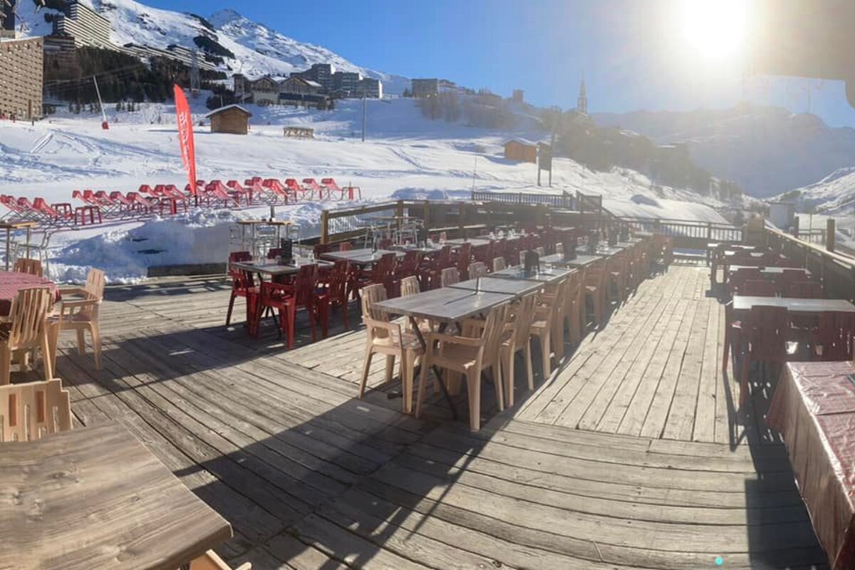 A wooden deck with tables and chairs in front of a snowy mountain