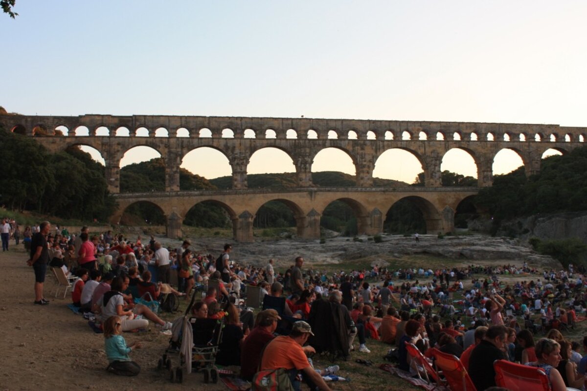 crowds of people on the riverbank at the pont du gard
