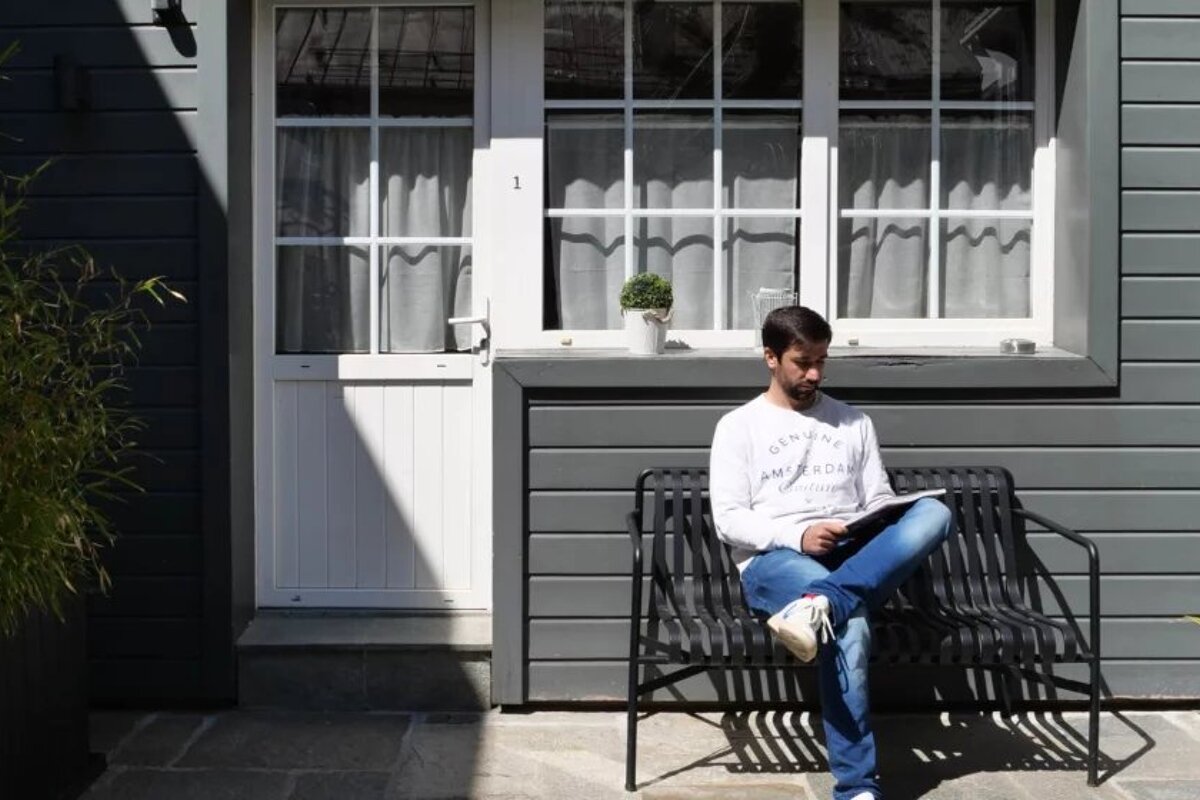 A man sits on a bench in front of a door that has the number 1 on it