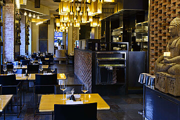 A stylish, dimly lit restaurant interior. Features modern tables, brick walls, unique suspended lighting, and a serene Buddha statue, creating an Asian-inspired ambiance.