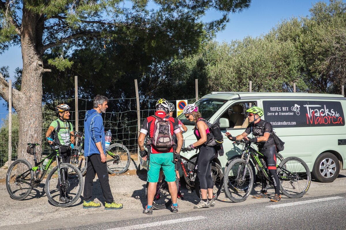 A group of cyclists are standing in front of a van that says tracks de mallorca