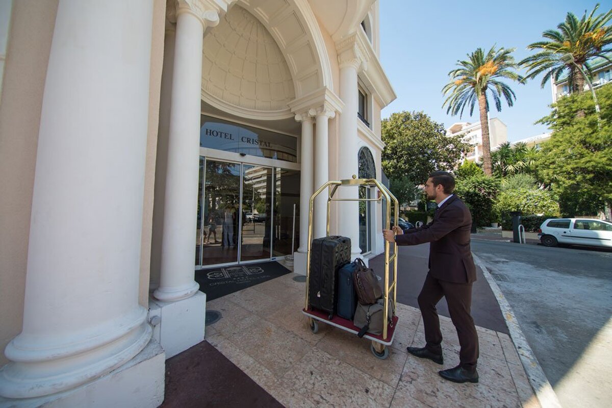A man pushes a luggage cart in front of the hotel creste