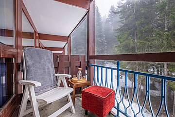 A balcony with a white chair and a red ottoman