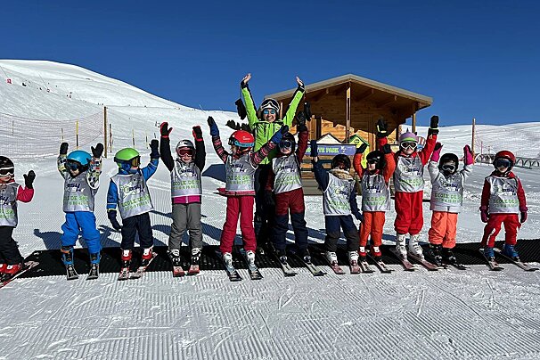 A group of young skiers are posing for a picture with their arms in the air
