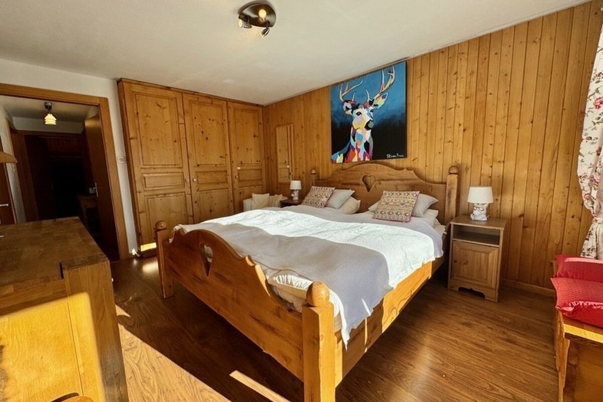 A rustic bedroom featuring wood paneling, a large wooden bed, and a colorful painting of a deer above the headboard.