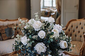 A vase filled with white roses and greenery sits on a table