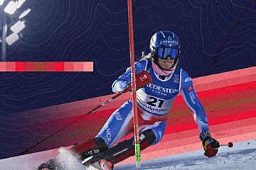 A female alpine skier in a blue suit and helmet navigates a course, kicking up snow. The background features blue contour lines and red stripes.