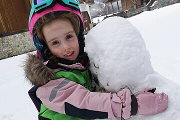 A little girl wearing a pink jacket and gloves holds a snowball