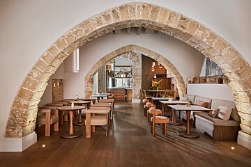Modern restaurant with ancient stone arches, stylish wooden tables, and comfortable seating. Hardwood floors complete the warm, inviting interior.