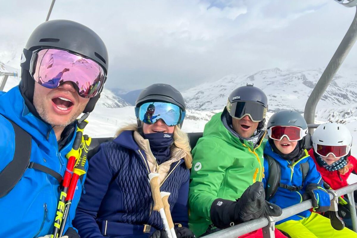 A group of people riding a ski lift with one wearing a leki jacket