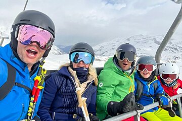 A group of people riding a ski lift with one wearing a leki jacket