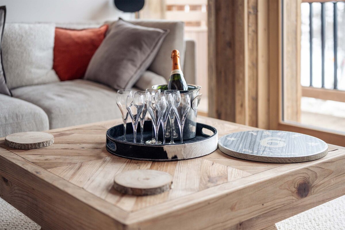 A bottle of champagne sits in a bucket of glasses on a wooden table