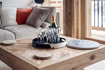 A bottle of champagne sits in a bucket of glasses on a wooden table