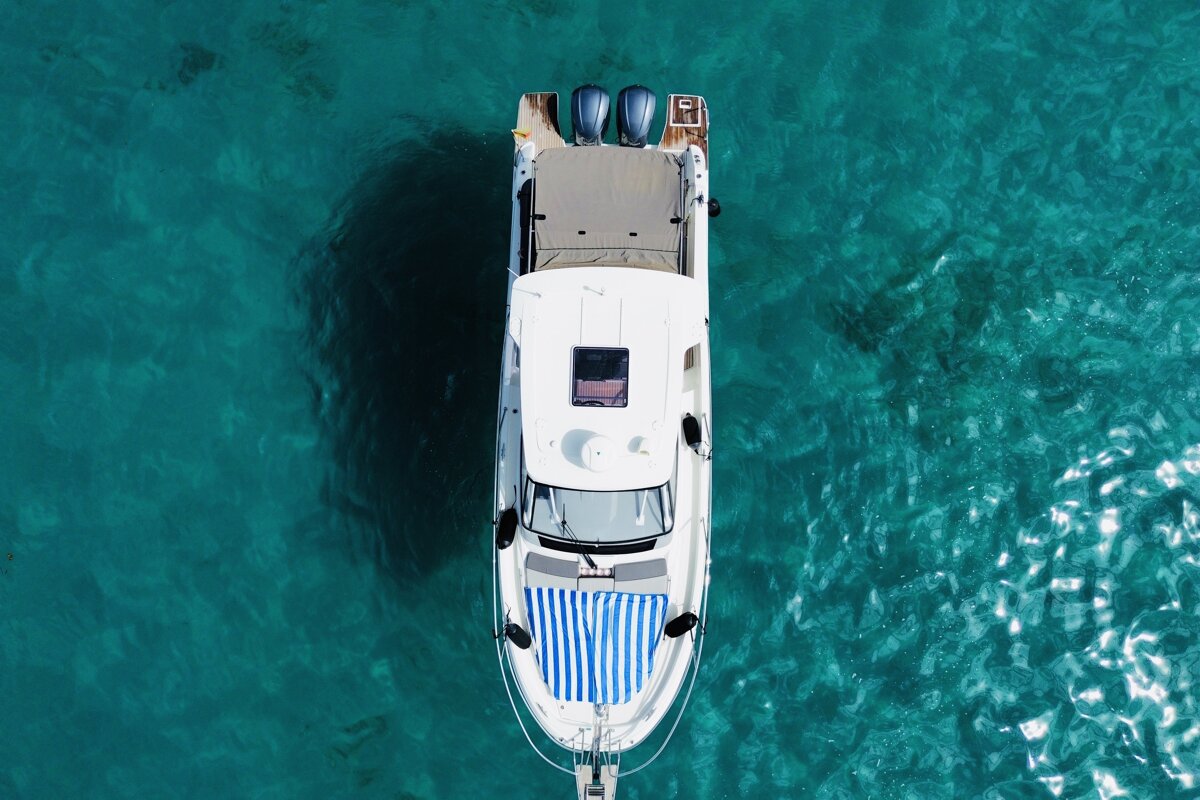 Aerial view of a white boat with blue motors and a striped towel, floating on crystal clear turquoise water.