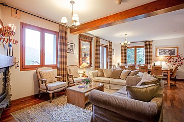 A cozy, rustic open-plan living and dining area with neutral sofas, wood beams, plaid curtains, and a dining table, offering a warm chalet ambiance.
