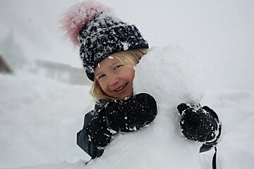 A little girl wearing a hat and mittens is playing in the snow