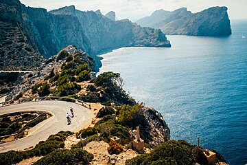 Two people riding bikes down a road near the ocean