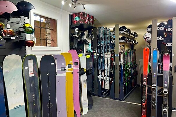A vibrant ski and snowboard shop interior. Colorful snowboards are displayed in the foreground, with racks of skis, helmets, and boots filling the store.
