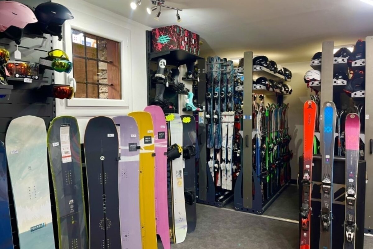A vibrant ski and snowboard shop interior. Colorful snowboards are displayed in the foreground, with racks of skis, helmets, and boots filling the store.