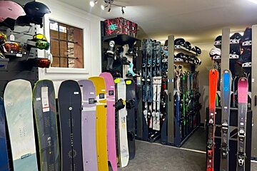 A vibrant ski and snowboard shop interior. Colorful snowboards are displayed in the foreground, with racks of skis, helmets, and boots filling the store.