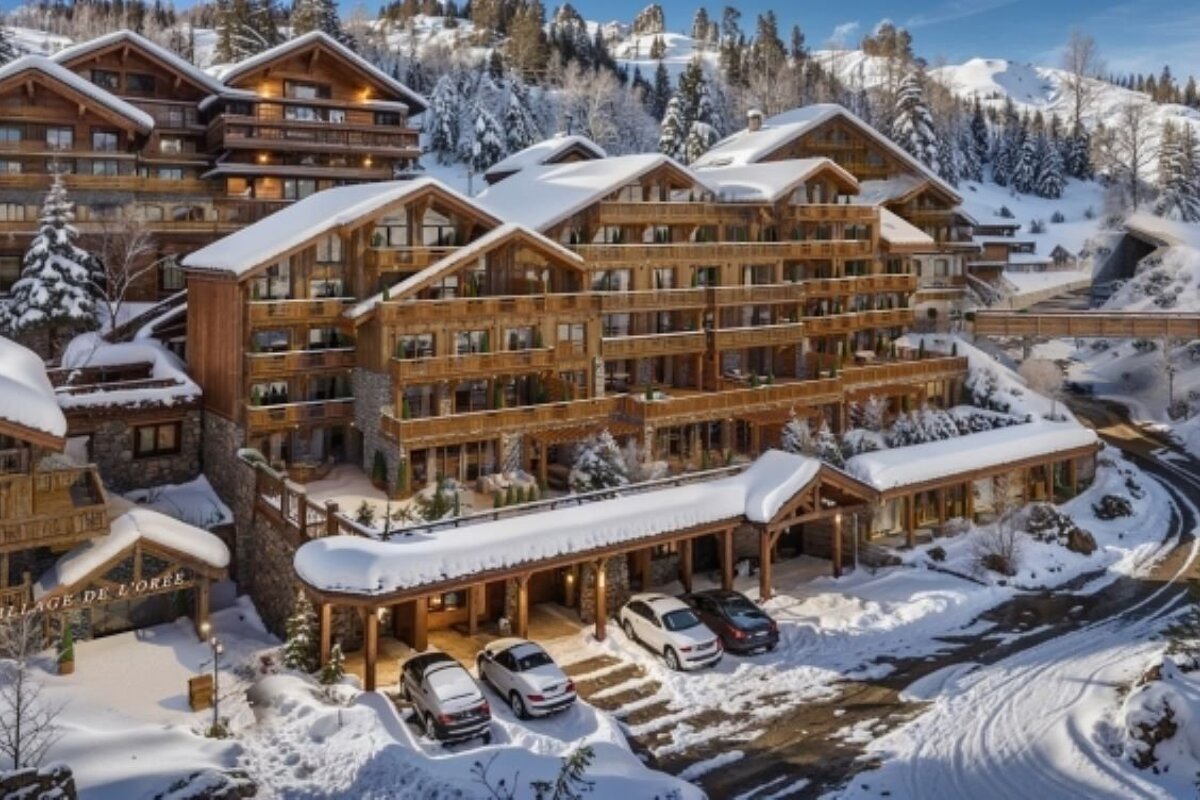 A beautiful, snow-covered wooden chalet resort nestled in snowy mountains, with cars parked at the entrance on a bright winter day.