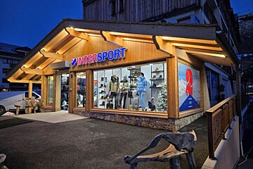 An illuminated Intersport store at night, featuring a wooden facade and winter sportswear displayed in its windows.