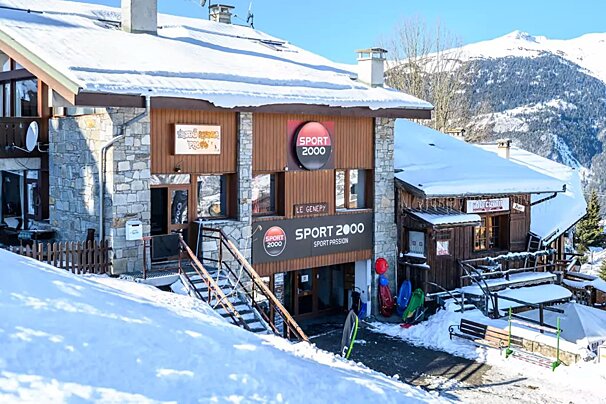 A snow-covered Sport 2000 store with a stone and wood facade in a snowy mountain ski resort. Sleds and ski equipment are visible outside.