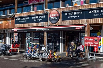 An Olivier Sports (Sport 2000) ski rental and sales shop. Equipment is displayed outside, and two people are seated on a bench.