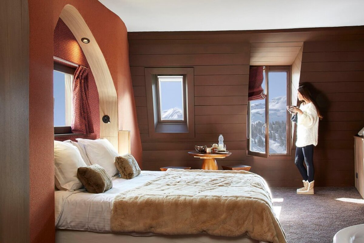 A woman stands in a bedroom looking out a window