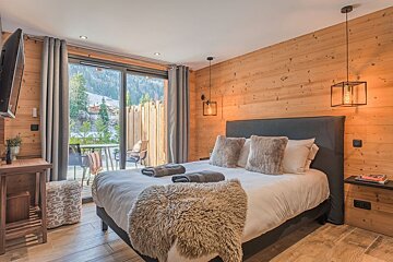Cozy, wood-paneled bedroom with a large bed, furry throw, and a snowy mountain view through sliding glass doors to a patio.