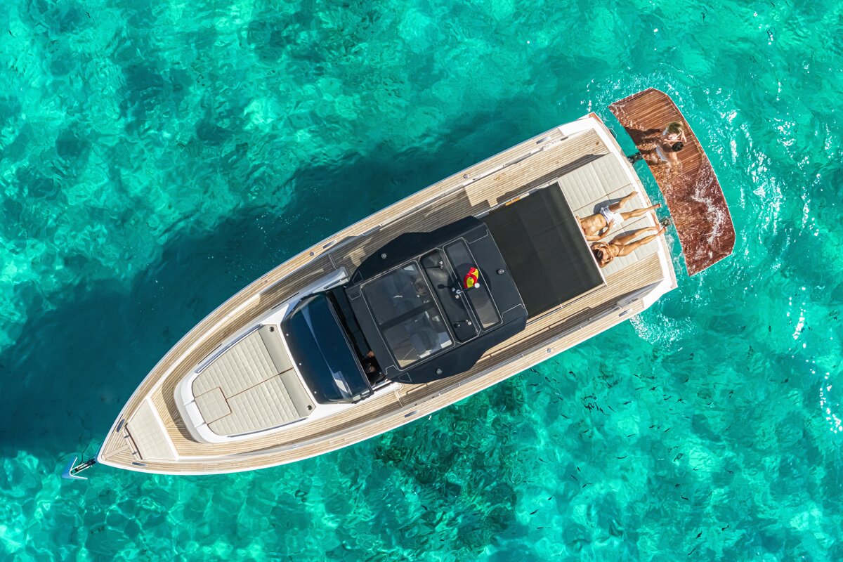 Aerial view of a luxury yacht in clear, turquoise water, with people sunbathing on the deck.