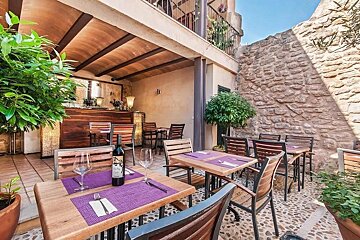 Inviting outdoor patio dining area with wooden tables, purple placemats, a wine bottle, stone walls, and lush greenery.
