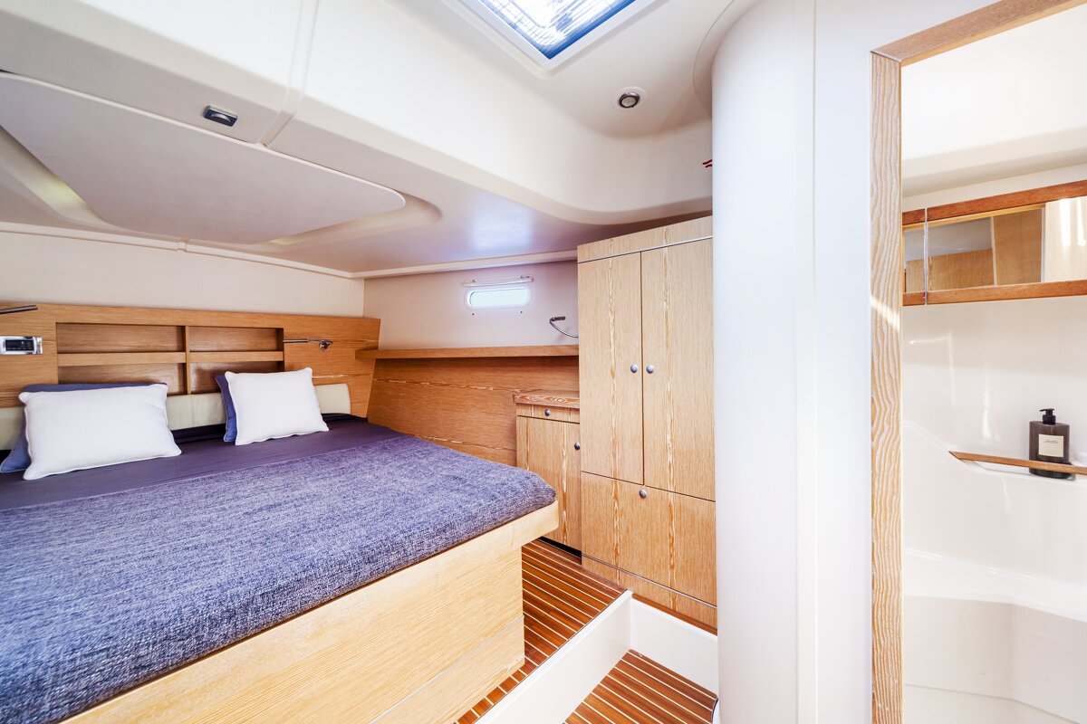 Modern yacht cabin with a double bed, light wood paneling, built-in wardrobe, and a view into the bathroom.