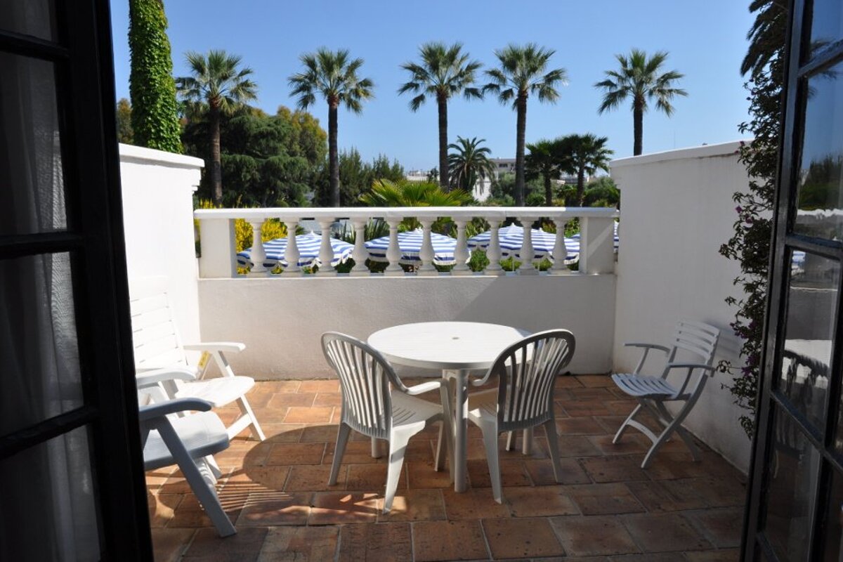 A patio with a table and chairs and palm trees in the background