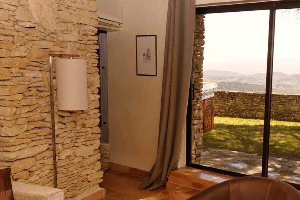 Stone walled room with brown leather arm chair and sliding doors onto terrace with country views