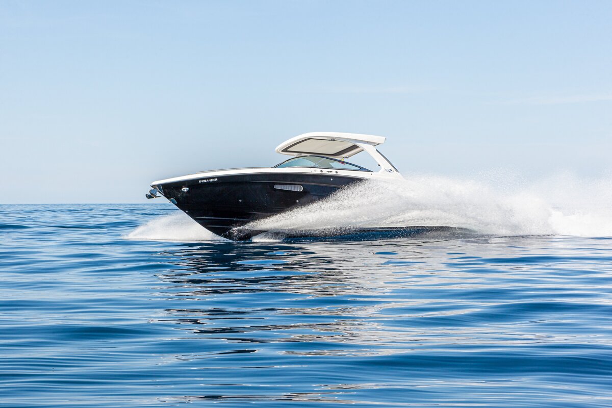 A sleek black and white speedboat glides rapidly across deep blue ocean water, creating a dramatic white spray.