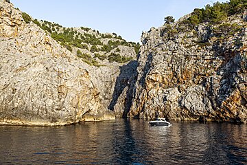 A small boat floats on calm water surrounded by towering rocky cliffs in a secluded cove.