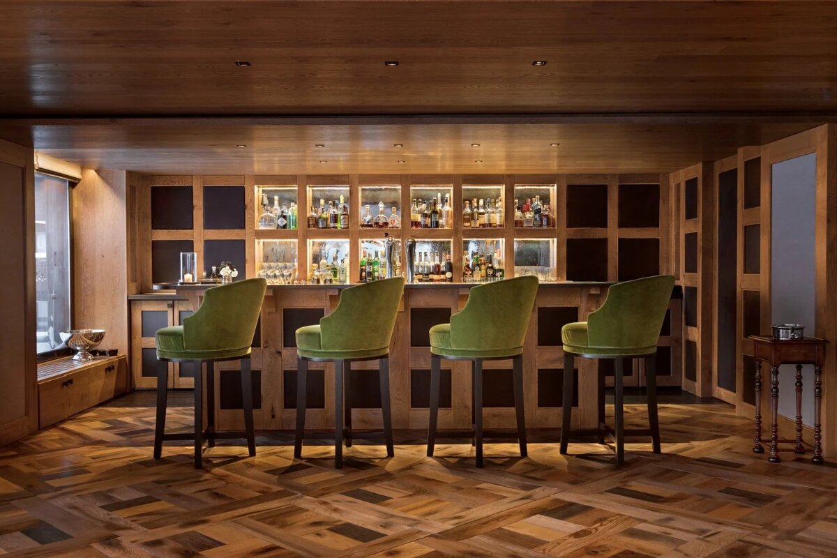 A bar with green chairs and bottles behind it