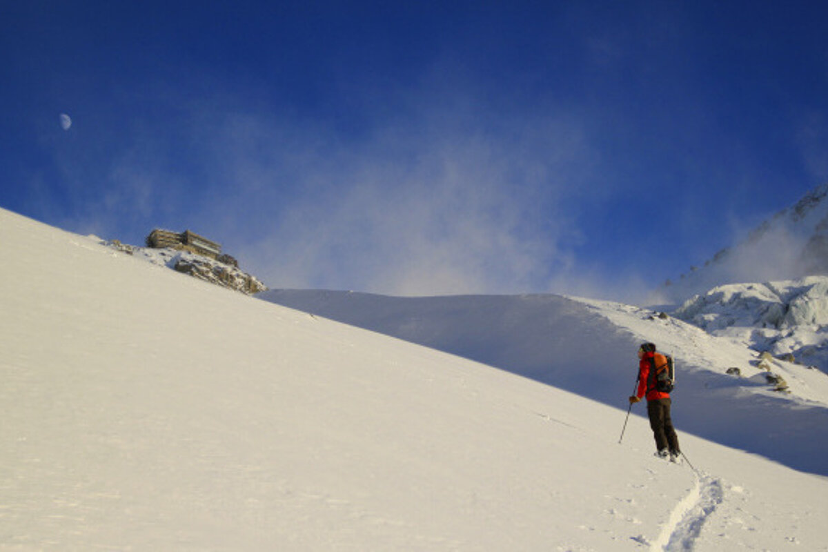 A person in a red jacket is walking up a snowy hill