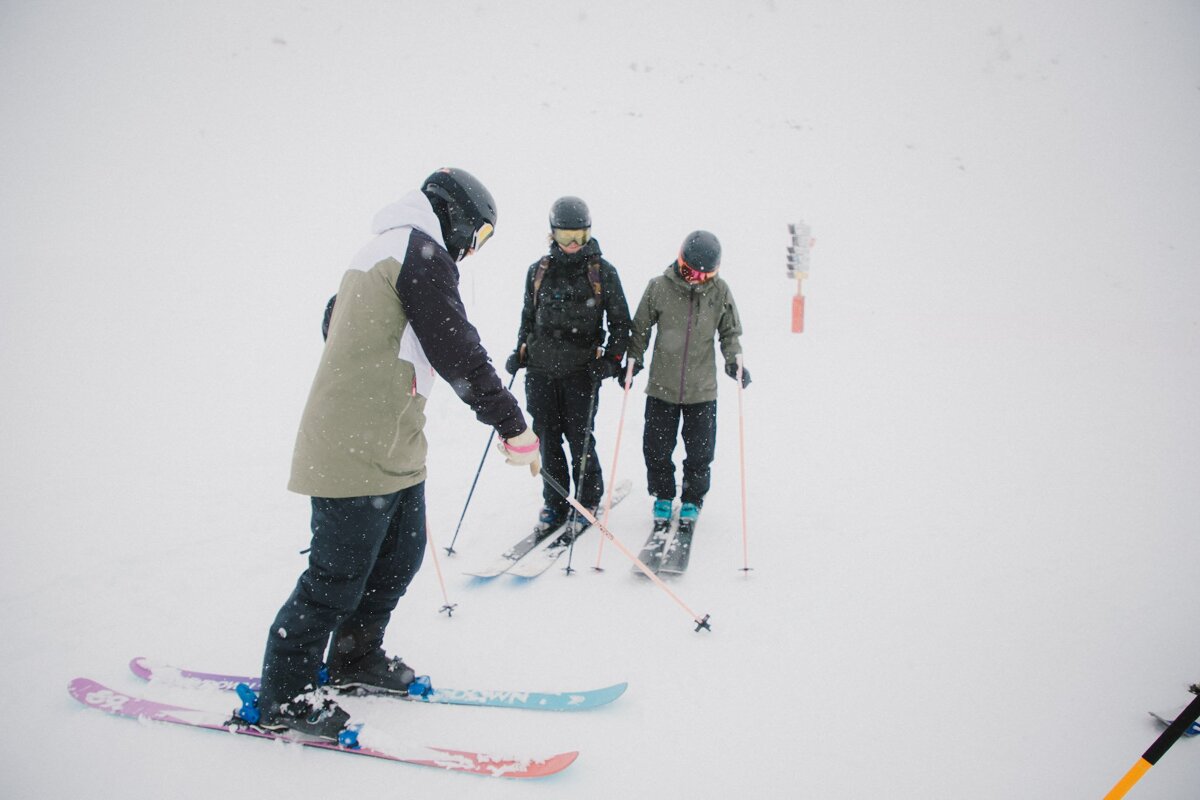 A group of skiers are standing on a snowy slope and one of them is wearing a purple ski