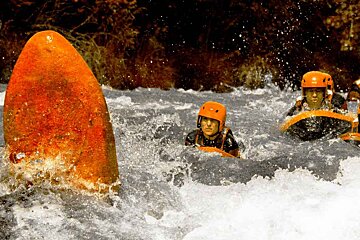 A man in an orange helmet is swimming in a river