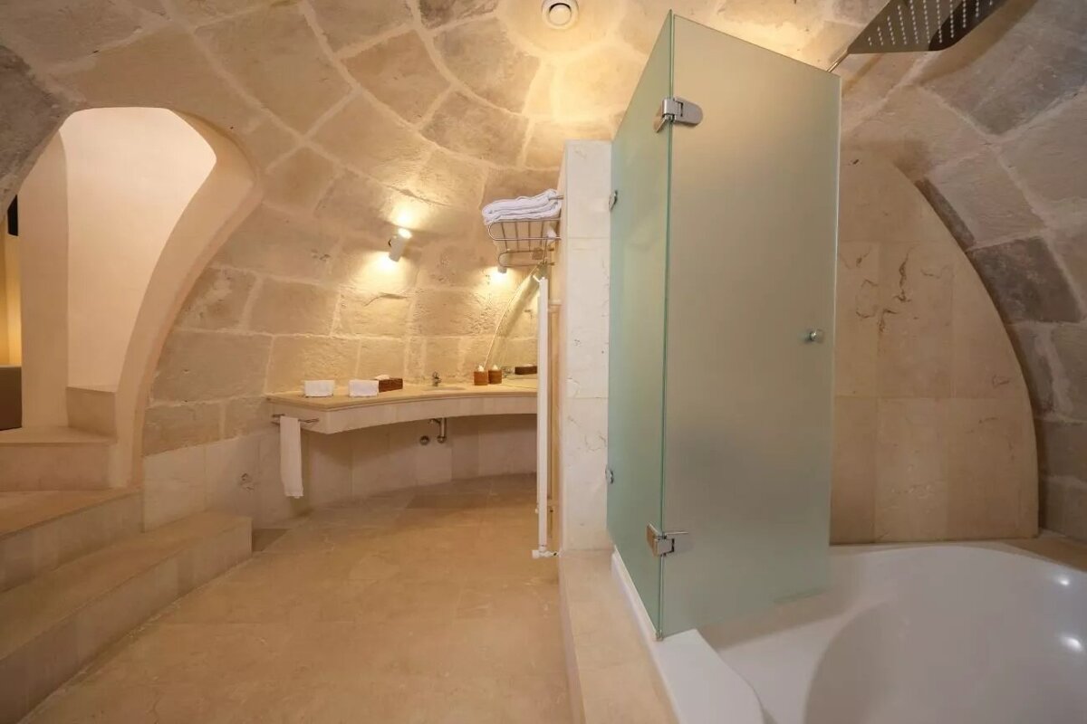 A luxurious, cave-style bathroom with rough stone walls, a domed ceiling, modern glass shower, and a curved vanity.