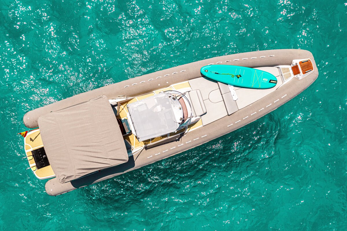 Aerial view of a motorboat with a turquoise paddleboard on its deck, floating on clear, vibrant turquoise water.