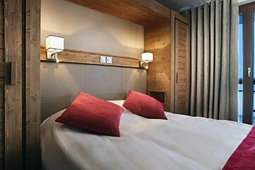 A hotel room with a bed and two red pillows