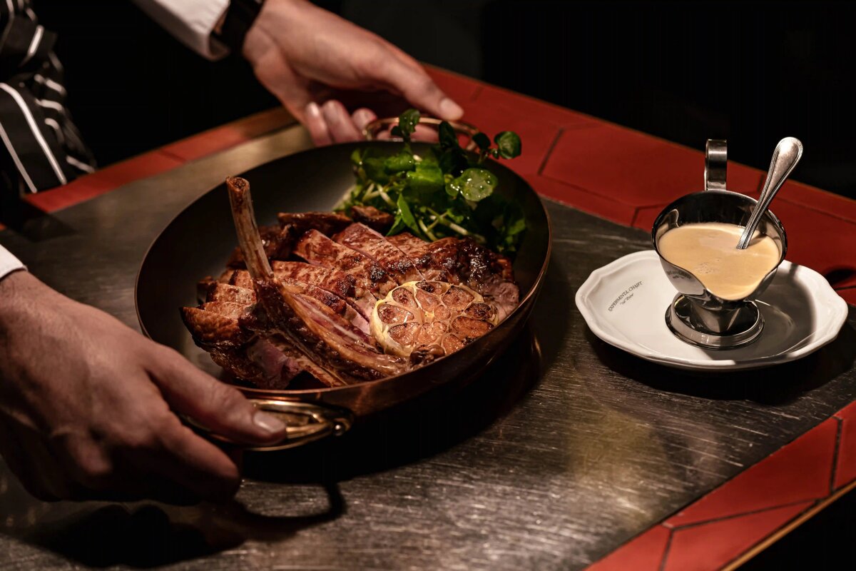 A person holding a pan of meat next to a cup of sauce