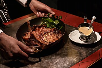 A person holding a pan of meat next to a cup of sauce